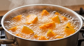 Olla de acero inoxidable con trozos de calabaza naranja hirviendo vigorosamente en mucha agua, con abundante vapor ascendiendo.