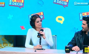 Mujer con auriculares y micrófono en una mesa, un hombre a su derecha. Fondo azul con gráficos de texto "Sin Qué Decir" y un número de teléfono