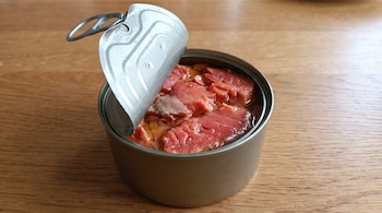Lata de salmón abierta con trozos de pescado en su jugo sobre una superficie de madera.