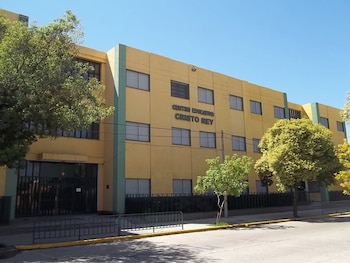 Fachada de un edificio amarillo de tres pisos con el cartel Centro Educativo Cristo Rey, ventanas y árboles junto a una calle