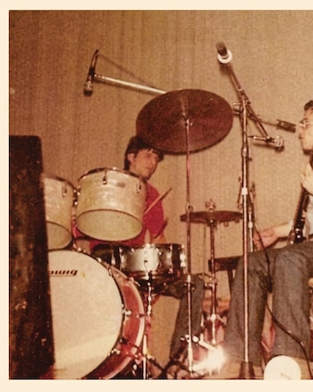 Tres jóvenes músicos en un interior, dos con guitarras eléctricas y uno sentado frente a un teclado, con una ventana al fondo