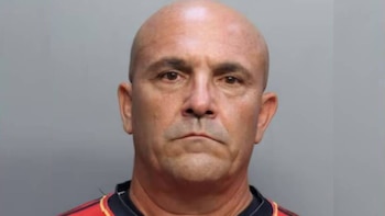 Fotografía de ficha policial de un hombre calvo con camiseta roja sobre un fondo gris
