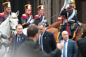 Grupo de hombres en traje oscuro y militares a caballo con uniformes de gala azul, rojo y dorado, en una procesión al aire libre