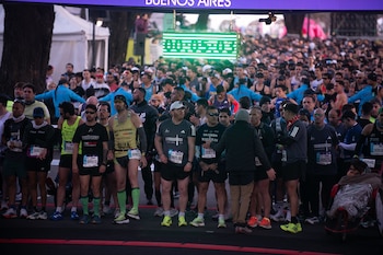 Una multitud de corredores con dorsales numerados espera alineada en la partida bajo un cronómetro digital verde