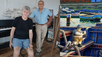 Dos hombres; uno sentado en un taburete con anteojos en mano, el otro de pie. Detrás, un piano y una escultura. A la derecha, un cuadro y una escultura de un personaje con un móvil