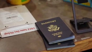 Primer plano de dos pasaportes de Estados Unidos apilados sobre una superficie de madera, con parte de un paquete que dice "FREE Same Day Pickup" a la izquierda