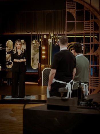 Wanda Nara, vestida de negro, de pie en un estudio de televisión. Dos hombres, identificados como Maxi López y Turco Husain, le dan la espalda