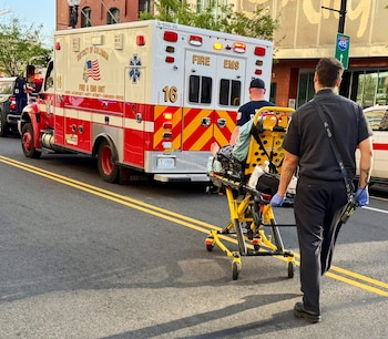 Un vehículo de Bomberos y EMS del Distrito de Columbia estacionado mientras dos paramédicos trasladan a un paciente en camilla por la calle