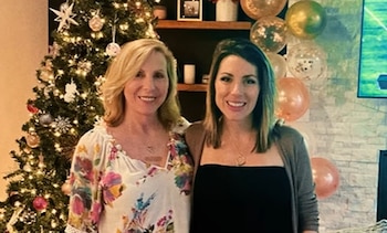 Dos mujeres posan de pie junto a un árbol de Navidad iluminado y un arreglo de globos decorativos