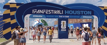 Gente entra al FIFA Fan Festival Houston 2026 bajo un arco azul; un balón inflable y señales del Mundial 2026 son visibles