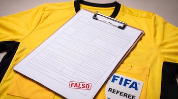 Camiseta amarilla con insignia de árbitro de la FIFA y una tabla con un formulario impreso que lleva un sello rojo con la palabra falso.
