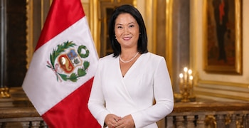Keiko Fujimori con blazer blanco y collar de perlas posa frente a la bandera de Perú y un fondo de interior palaciego con candelabros y cuadros