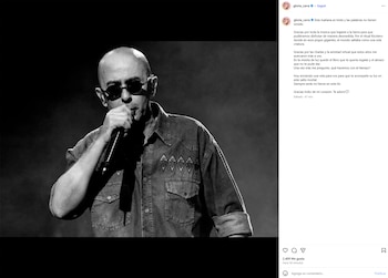 Fotografía en blanco y negro de Indio Solari, un hombre calvo con gafas de sol, cantando en un micrófono en el escenario, vistiendo una camisa de jean