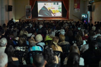 Público sentado en un auditorio a oscuras mientras observa una pantalla gigante instalada sobre un escenario