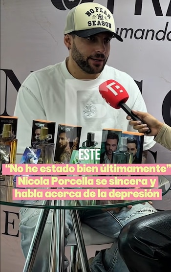 Nicola Porcella con gorra y camiseta blanca habla ante un micrófono frente a varios frascos de perfume sobre una mesa de vidrio