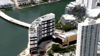 Vista aérea de un área urbana con rascacielos y edificios de gran altura junto a un canal de agua. Un puente blanco curvo y un edificio blanco y negro son visibles