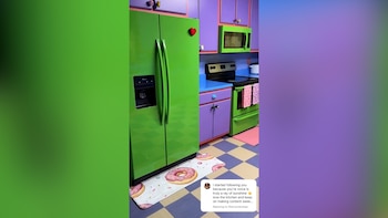 Cocina con refrigerador y horno verdes brillantes, microondas verde, gabinetes morados, encimeras azules y piso a cuadros. Un tapete con donas rosadas está frente al refrigerador