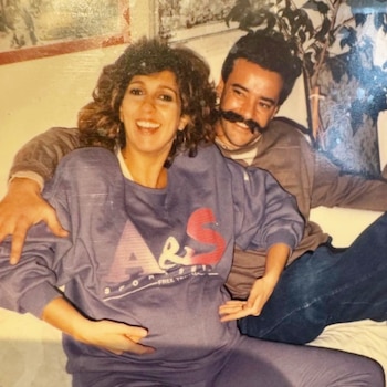 Fotografía de una mujer sonriente y embarazada junto a un hombre con bigote que la rodea con el brazo
