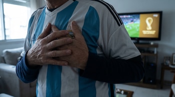 Torso con camiseta argentina de franjas celestes y blancas, manos sobre el pecho. Al fondo, una TV borrosa muestra un partido de fútbol con el logo del Mundial.