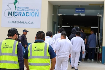 Trabajadores con chalecos amarillos del Instituto Guatemalteco de Migración observan a un grupo de personas ingresar a un edificio bajo un letrero de "INGRESO"