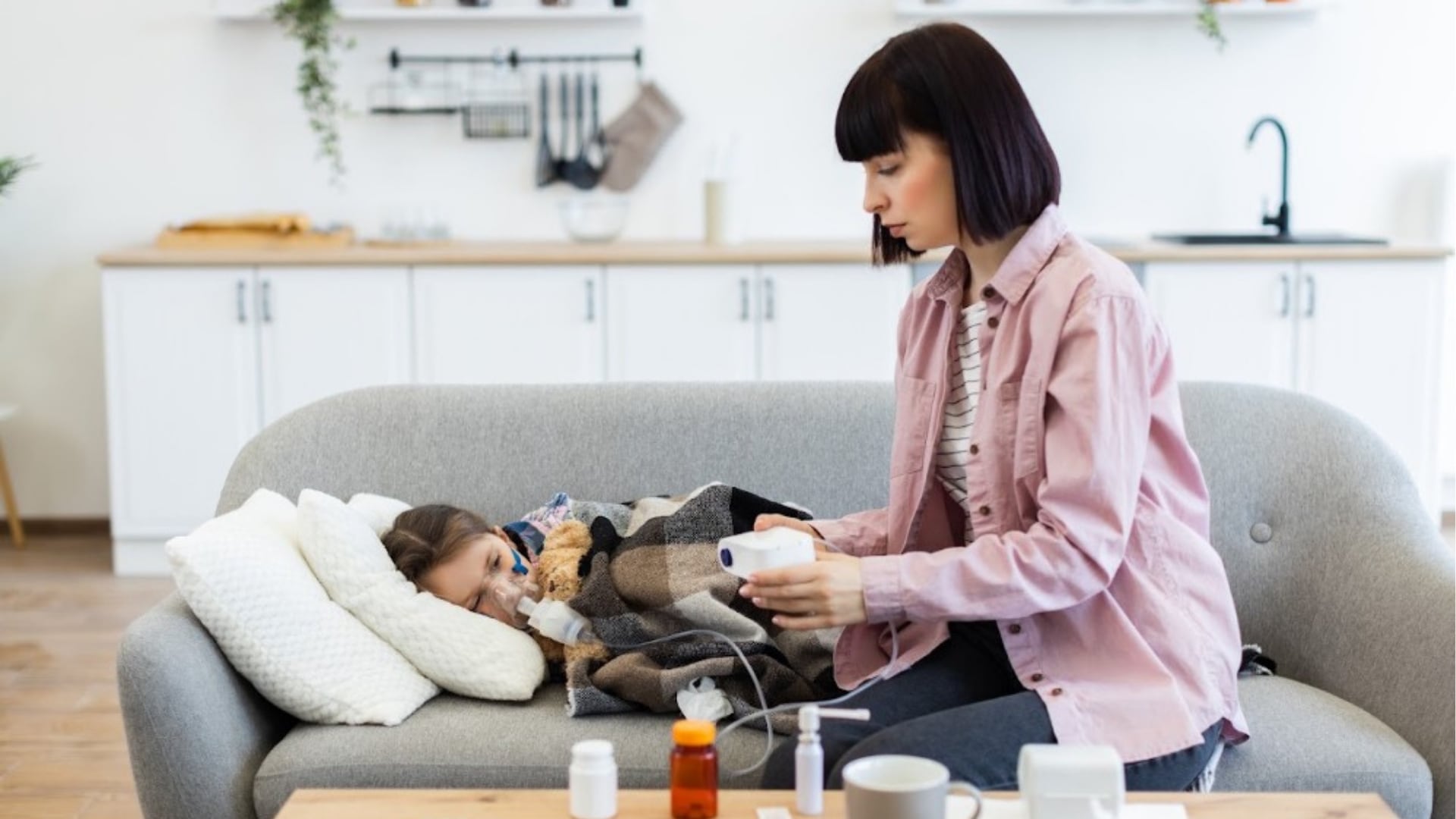 Una mujer utiliza un nebulizador para administrar un tratamiento respiratorio a una niña recostada en un sofá.