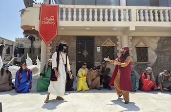 Un grupo de actores vestidos con túnicas y sandalias, representando una escena teatral al aire libre frente a una edificación de piedra del Castillo de Chancay
