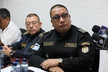 Un hombre con uniforme policial negro, anteojos y la insignia de Esvin Jacinto permanece sentado frente a varios micrófonos de prensa