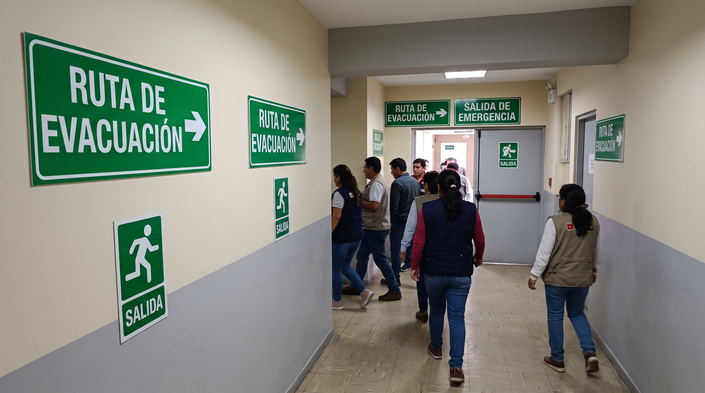 Varias personas recorren el pasillo de un edificio público en Perú según la señalética de ruta de evacuación que las guía hacia la salida de emergencia. (Imagen Ilustrativa Infobae)
