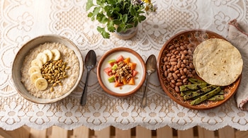 Tres recipientes con avena con plátano y pepitas, jocoque con fruta picada y un plato con frijoles, nopales asados y tortillas de maíz.