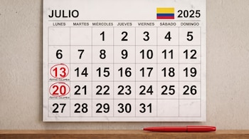 Calendario del mes de julio de 2025 con la bandera de Colombia, los días 13 y 20 marcados como festivos y una pluma roja en primer plano sobre una mesa de madera.