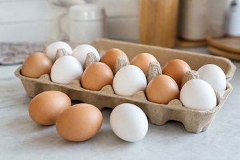 Huevos blancos y marrones dentro de un envase de cartón y tres huevos sobre una encimera de mármol.