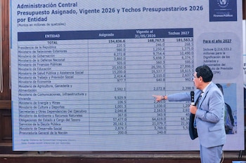 Una persona con traje gris apunta a una pantalla con una tabla de presupuestos de entidades gubernamentales de Guatemala, en montos de quetzales