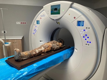 Momia de un niño envuelta en textiles con patrones yace en la camilla de un escáner CT Canon Aquilion Prime SP blanco en una sala de examen