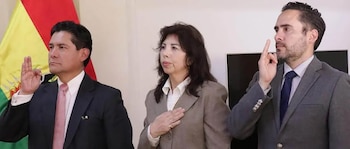 Dos hombres y una mujer vestidos formalmente realizan el juramento de posesión frente a la bandera de Bolivia