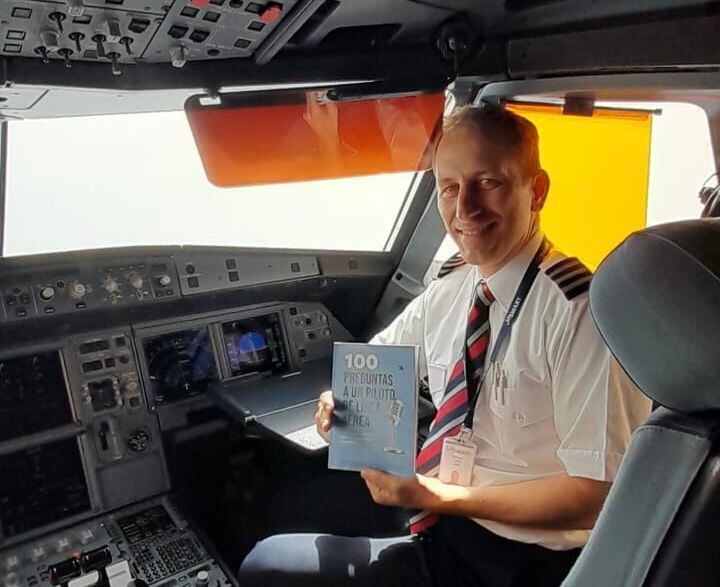Un piloto sonriente posa en la cabina de un avión con su libro