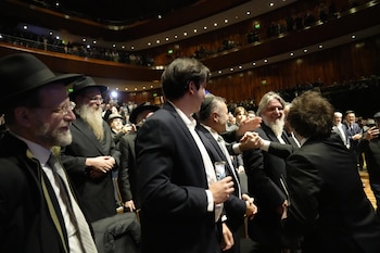 Javier Milei saluda a un hombre barbudo en un evento formal. Otros asistentes con vestimenta tradicional judía y público en el auditorio de fondo