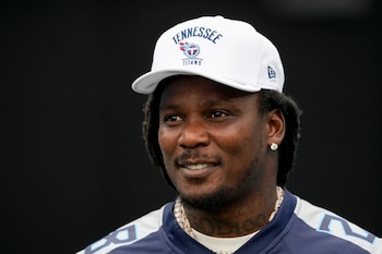 Primer plano de un hombre con gorra blanca de los Tennessee Titans, camiseta deportiva azul, cadenas y un pendiente dorado