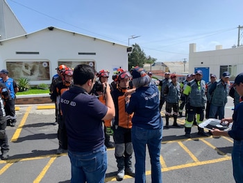 Grupo de personas en un exterior. Incluye rescatistas con uniformes naranjas y negros, cascos y chalecos. Hay dos individuos con camisetas 'SE-CONRED'