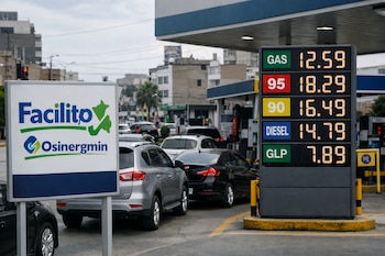 Estación de servicio urbana con fila de vehículos, un cartel digital muestra precios de combustibles y un letrero con logos Facilito y Osinergmin.