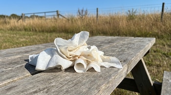 Un montón de toallitas húmedas secas y arrugadas, de color blanco y crema, sobre una mesa de pícnic de madera rústica bajo un cielo azul claro.