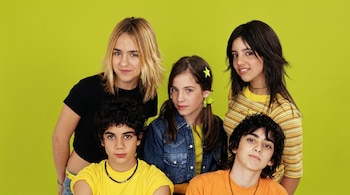 Cinco jóvenes posan para una fotografía con un fondo verde. Hay dos chicas y un chico de pie, y dos chicos sentados. Visten ropa informal.
