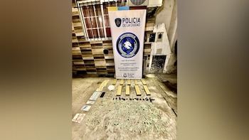 Bandera de la Policía de la Ciudad, billetes, un teléfono móvil, bloques rectangulares, pequeños paquetes verdes y substancias oscuras sobre el suelo