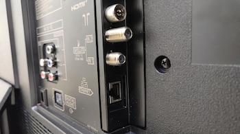 Parte trasera de un televisor con puertos HDMI, AV in, satélite in 1 y 2, digital audio y ethernet, más un tornillo y plástico negro texturizado.