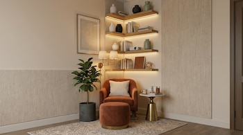 Un rincón de sala con un sillón color terracota y un puf, una planta alta, estanterías de madera con luces LED que muestran libros y jarrones, y una mesa auxiliar dorada.