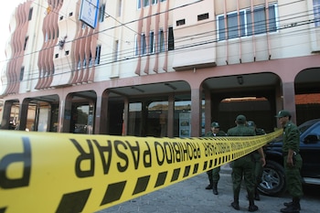Edificio de hotel con fachada, un cartel con la palabra 'HOTEL'. Cinta amarilla con la inscripción 'PROHIBIDO PASAR' y agentes de seguridad uniformados detrás