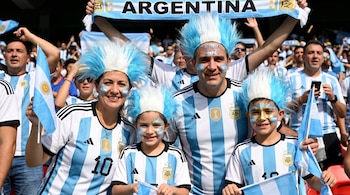 Una familia argentina sonriente con camisetas, pelucas celestes y blancas, maquillaje facial y banderas. Al fondo, una pancarta de "ARGENTINA".