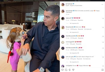 Cristiano Ronaldo en camisa oscura, mirando a su hija Bella Esmeralda, quien lleva un traje rosa, trenzas y una máscara de muñeca aterradora en Halloween