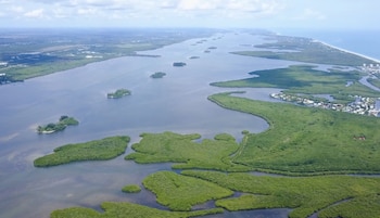 Fotografía aérea de la laguna Indian River, mostrando islas fluviales y marismas verdes, así como una franja costera con edificios bajo un cielo nublado