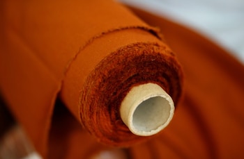 Primer plano de un rollo de tela de poliéster reciclado color naranja rojizo sobre un núcleo de cartón, con el borde visible y una textura fibrosa
