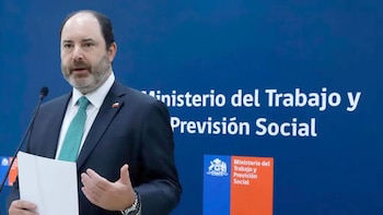 Hombre con barba y traje oscuro, corbata verde, hablando en un micrófono. Detrás, un panel azul con el logo del Ministerio del Trabajo y Previsión Social de Chile